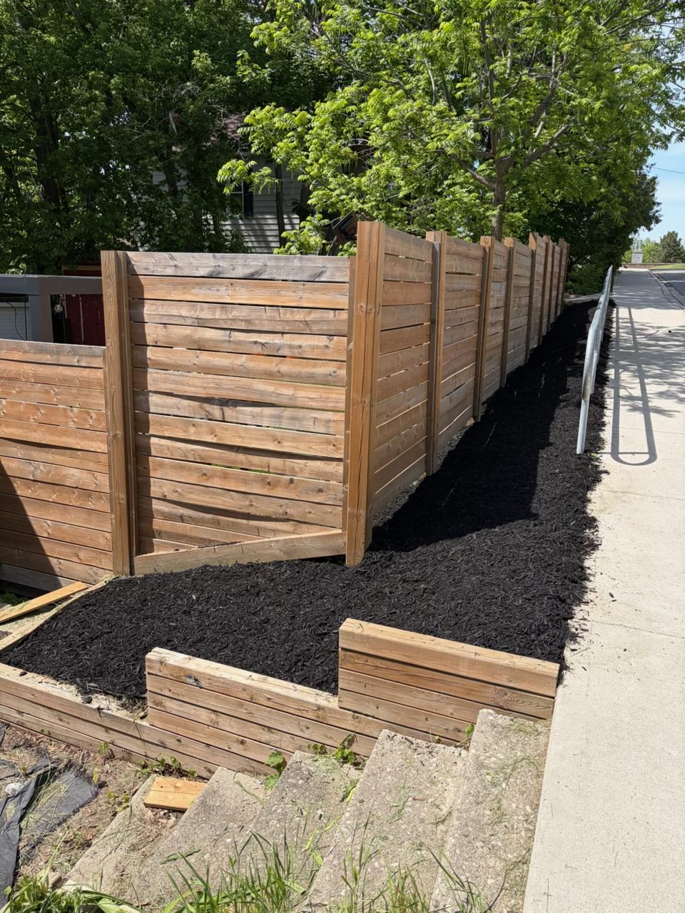 Cedar fence with fresh black mulch bed and timber retaining wall